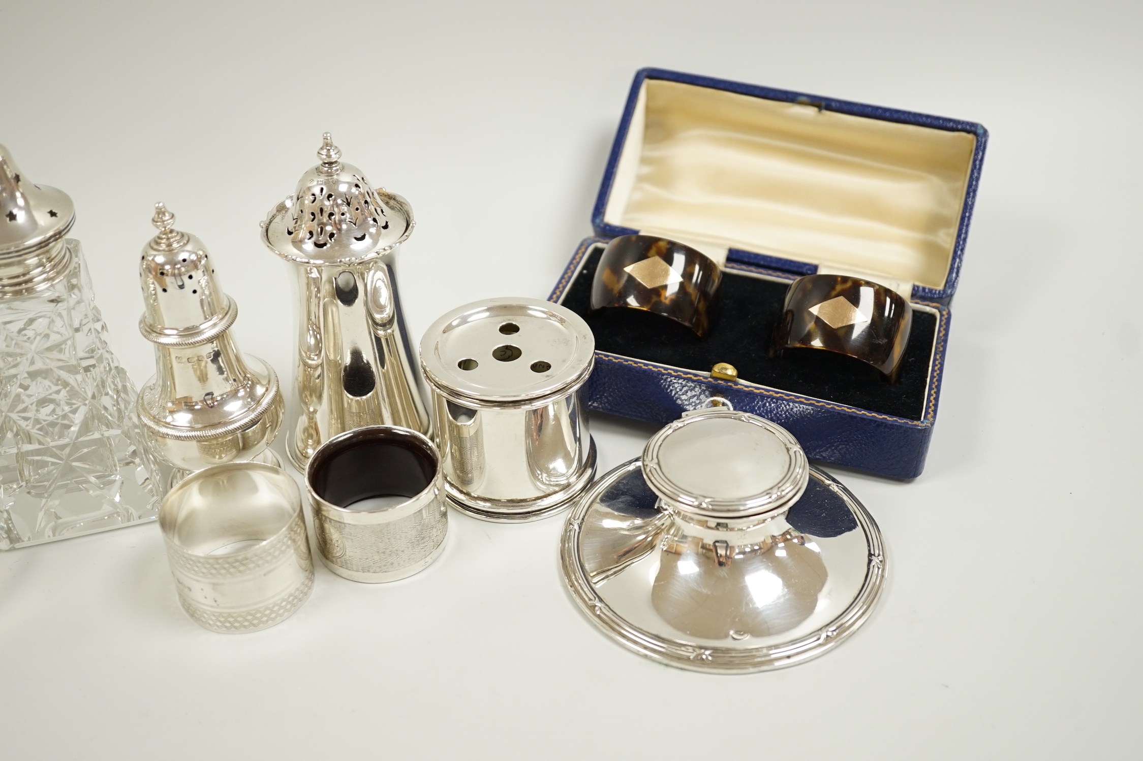 A group of mixed silver including three sugar casters, two inkwells, two pairs of napkin rings (one tortoiseshell) and a white metal box and cover.